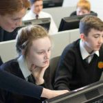 Teacher helps student in computer class in Irish high school
